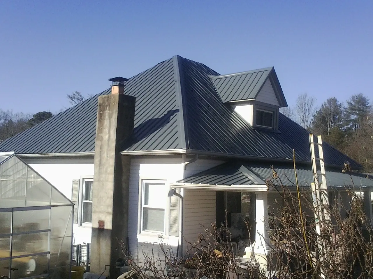 Dark blue standing seam metal roof on a white farmhouse with dormer — Slate & Tile Roof Repair by Roofing Brothers in Colonia