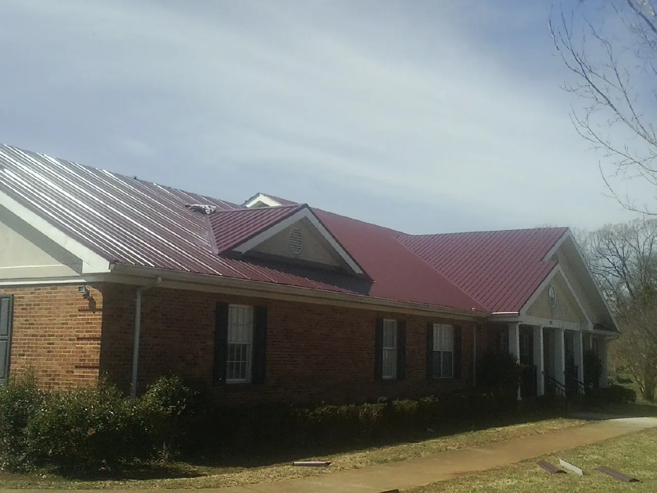 Red metal roof with gabled entries on a long brick building, from a Hail Damage Roof Repair job in Colonia