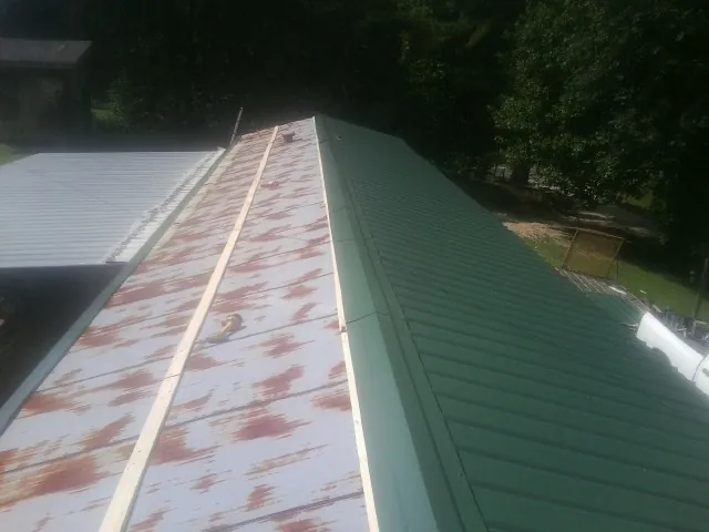 Old rusted panels beside newly installed green metal roofing — Wind Damage Roof Repair by Roofing Brothers in Colonia