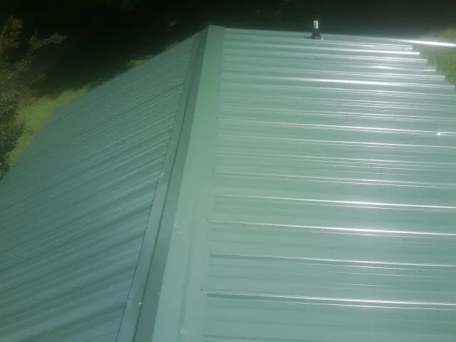New green metal panels meeting at the ridge of a roof — Flat Roof Repair work by our crew in Colonia