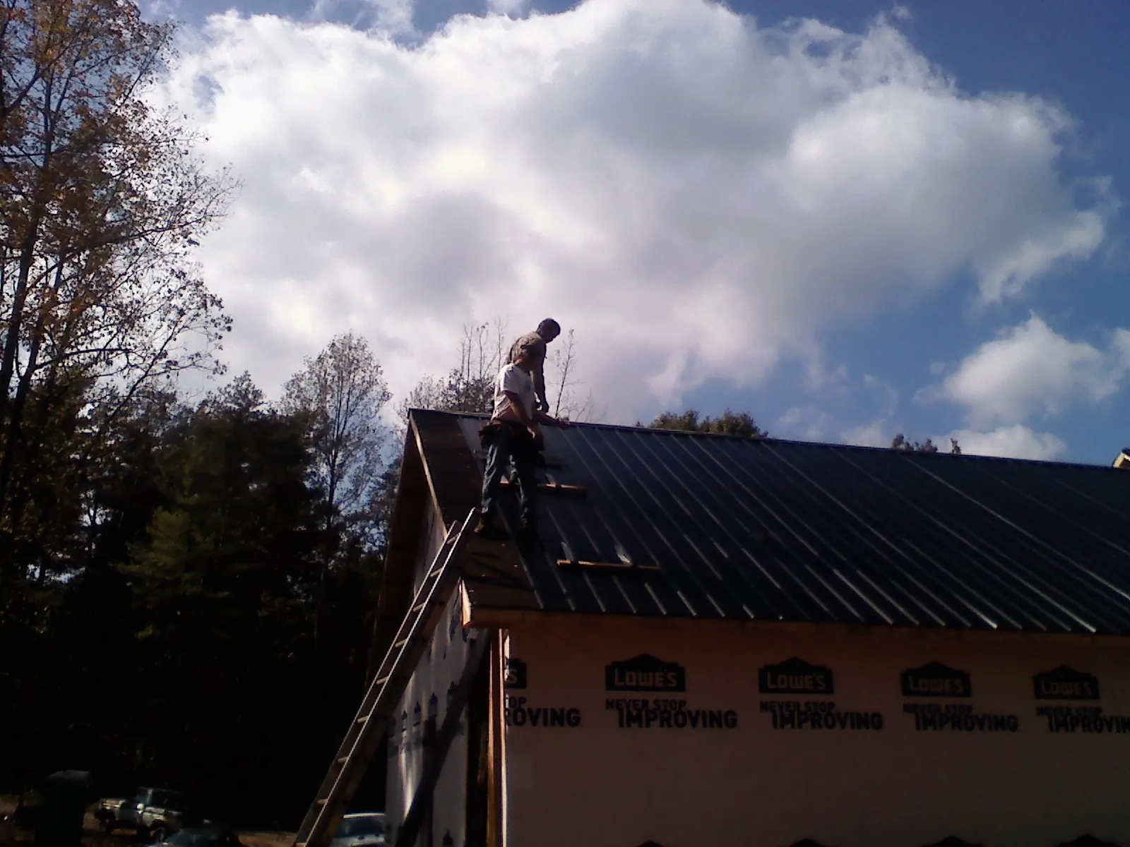 Roofer fastening dark metal panels high against a cloudy sky, from a Roof Inspection job in Colonia