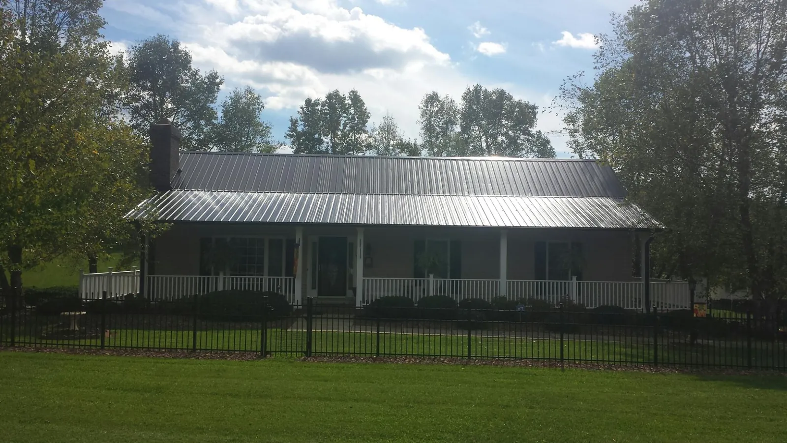 Gray metal roof on a brick ranch with a full width front porch — Gutter Guard Installation work by our crew in Colonia
