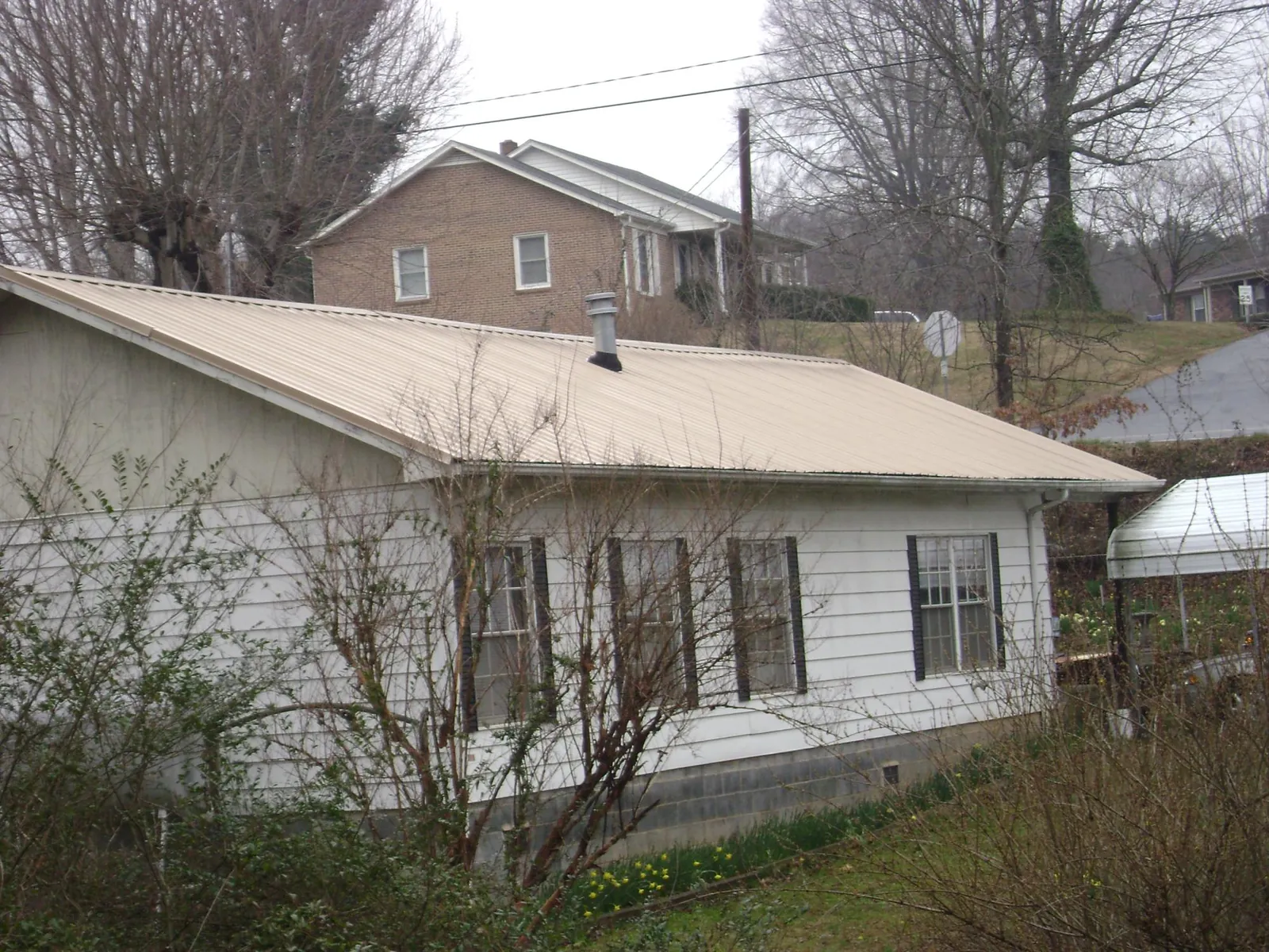 Tan metal roof on a white sided house set into a hillside — Commercial Roofing by Roofing Brothers in Colonia