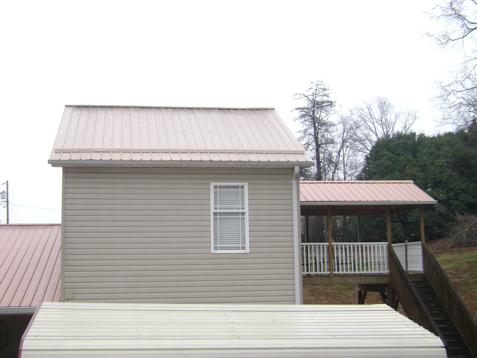 Tan metal roofs on a two story addition and attached porch, from a Roof Replacement job in Colonia
