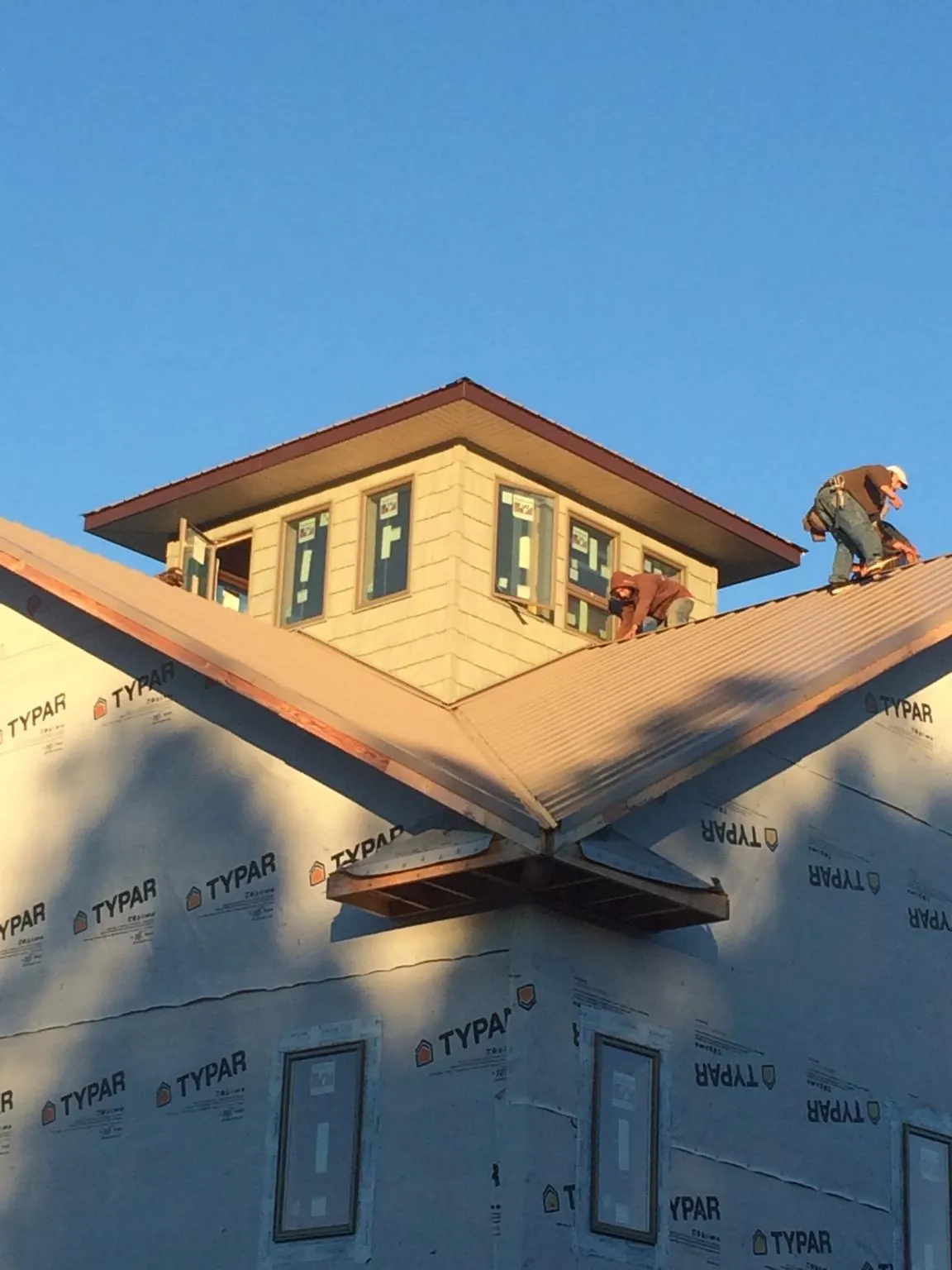 Roofers working around a rooftop cupola on a new metal roof at sunset — Roof Waterproofing in Colonia by Roofing Brothers